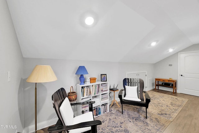 living area with vaulted ceiling, baseboards, and wood finished floors