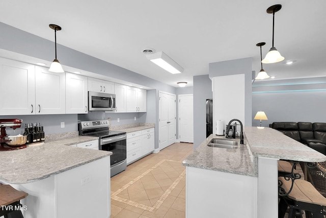 kitchen with a sink, a kitchen breakfast bar, white cabinets, appliances with stainless steel finishes, and pendant lighting