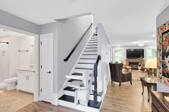 staircase with wood finished floors and a stone fireplace