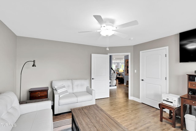 living room featuring light wood-style flooring, baseboards, and ceiling fan