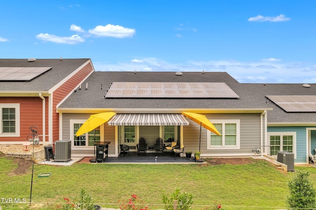 rear view of house featuring a patio area, a shingled roof, roof mounted solar panels, and cooling unit