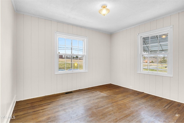 spare room featuring a healthy amount of sunlight, visible vents, wood finished floors, and ornamental molding