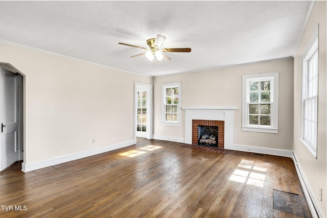 unfurnished living room with dark wood-type flooring, a brick fireplace, a healthy amount of sunlight, and baseboards