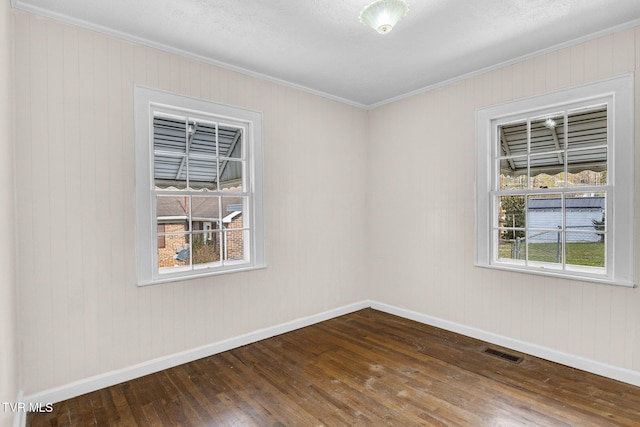 spare room featuring baseboards, dark wood-style flooring, visible vents, and crown molding