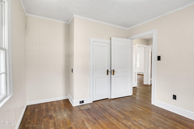 unfurnished bedroom with dark wood-type flooring, crown molding, and baseboards