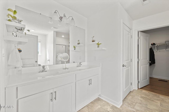 bathroom with a spacious closet, double vanity, a sink, and baseboards