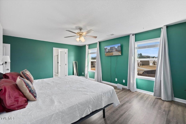 bedroom with ceiling fan, a textured ceiling, wood finished floors, visible vents, and baseboards