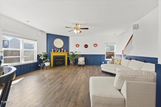 living room with a wainscoted wall, a fireplace, ceiling fan, wood finished floors, and stairs