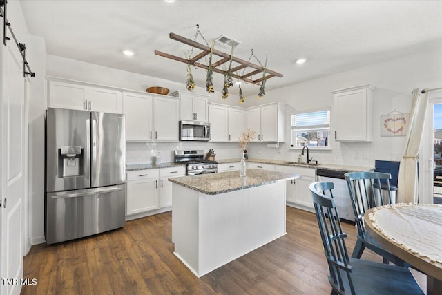 kitchen featuring a barn door, appliances with stainless steel finishes, white cabinets, and a center island