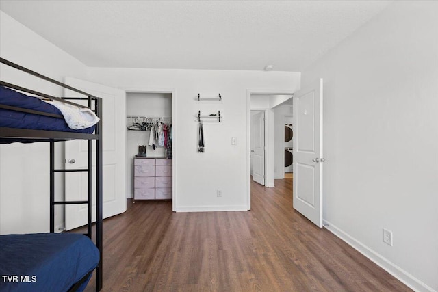 unfurnished bedroom featuring dark wood-style floors, stacked washer / dryer, and baseboards