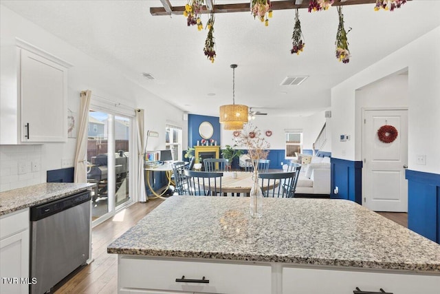 kitchen featuring visible vents, dishwasher, a kitchen island, light stone counters, and white cabinetry