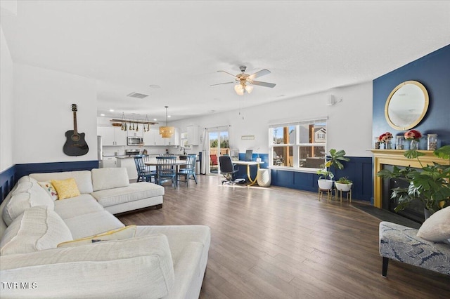 living room featuring ceiling fan, a fireplace, visible vents, and dark wood-type flooring