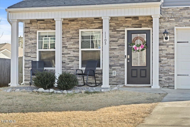 entrance to property with a porch, stone siding, a yard, and a shingled roof