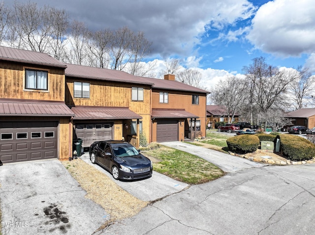 view of property with aphalt driveway, metal roof, a chimney, and a garage