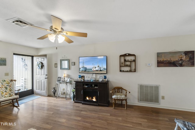 living area featuring baseboards, a lit fireplace, visible vents, and wood finished floors