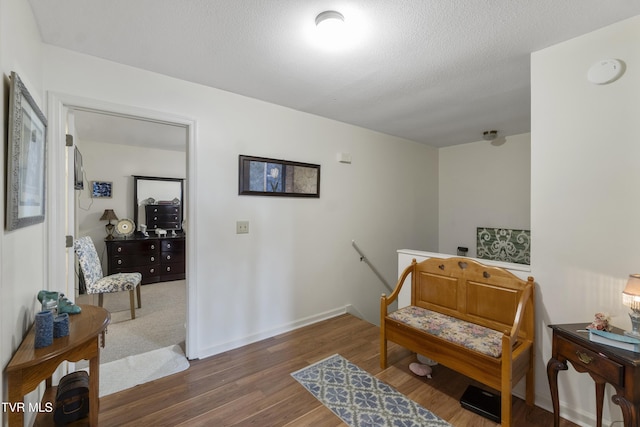 living area with a textured ceiling, wood finished floors, an upstairs landing, and baseboards