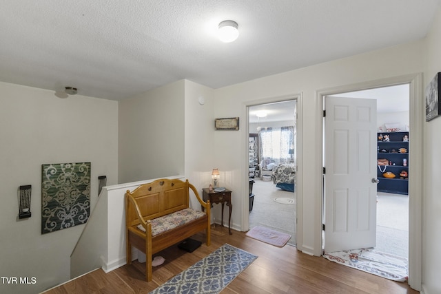 living area with a textured ceiling, wood finished floors, and an upstairs landing