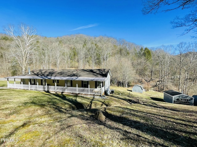 exterior space featuring a storage shed, a porch, an outdoor structure, and a view of trees