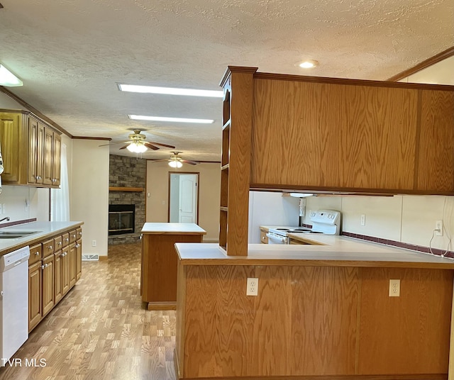 kitchen with light wood-style floors, brown cabinetry, a textured ceiling, white appliances, and a peninsula