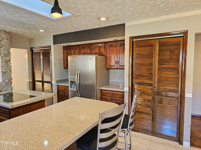 kitchen with stainless steel fridge with ice dispenser, a breakfast bar, black electric stovetop, light countertops, and a textured ceiling