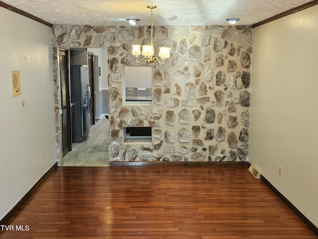 unfurnished dining area featuring visible vents, an inviting chandelier, a textured ceiling, wood finished floors, and baseboards