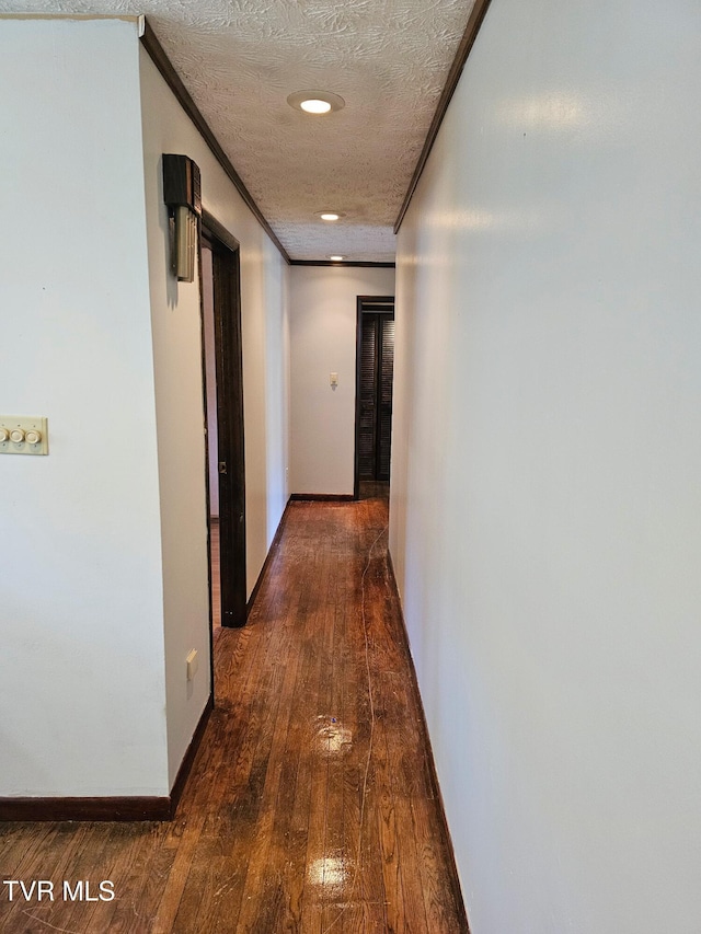 hallway with dark wood-style floors, baseboards, ornamental molding, and a textured ceiling