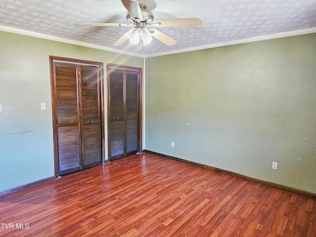 unfurnished bedroom with baseboards, two closets, a textured ceiling, and wood finished floors