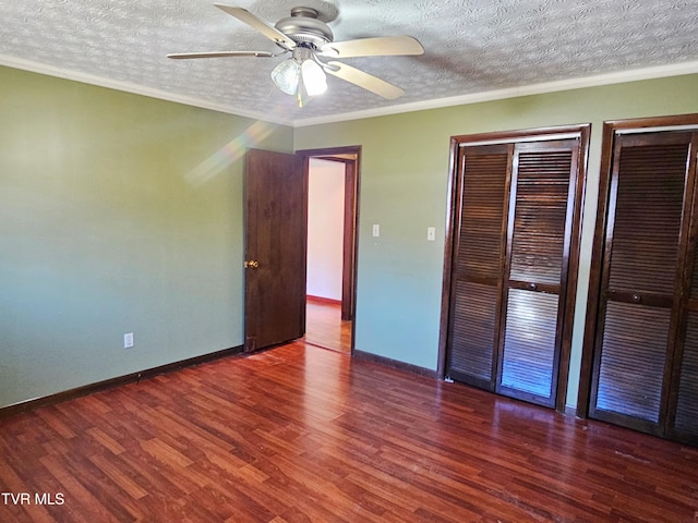 unfurnished bedroom with ornamental molding, dark wood-style flooring, two closets, and baseboards