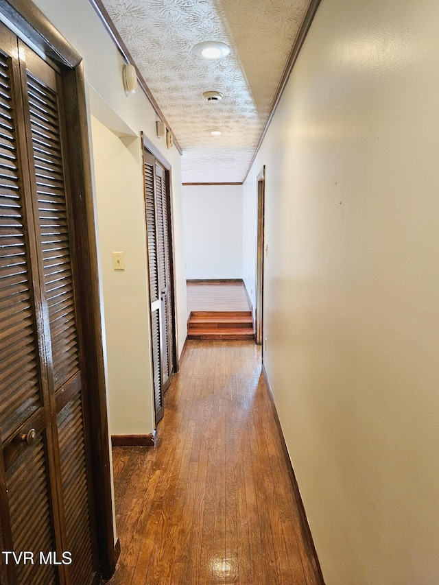 hallway featuring a textured ceiling, baseboards, dark wood-style floors, and crown molding