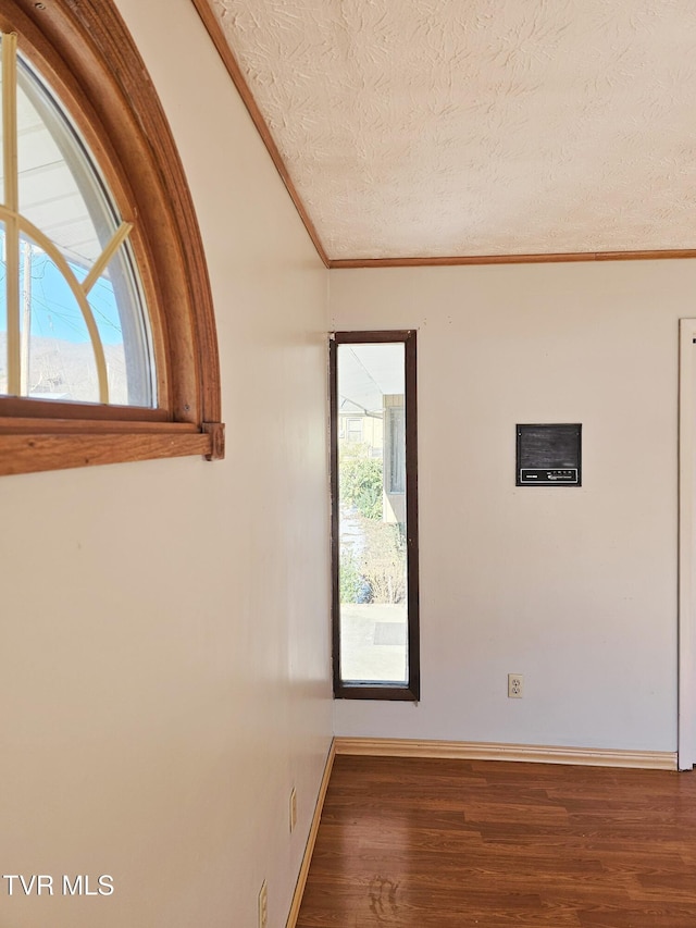 empty room with baseboards, a textured ceiling, ornamental molding, and wood finished floors