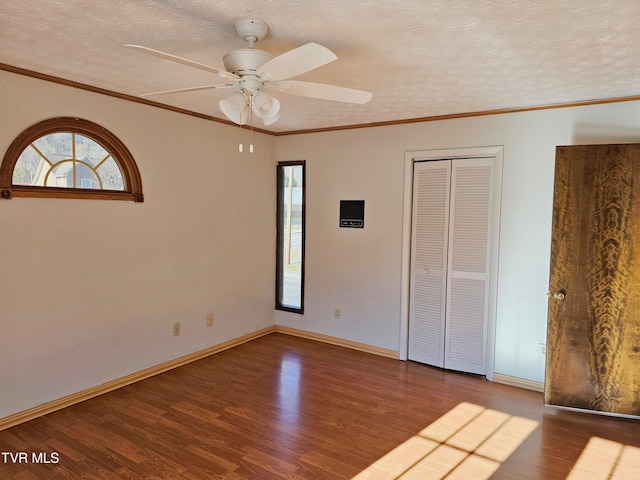 unfurnished bedroom with multiple windows, a textured ceiling, baseboards, and wood finished floors