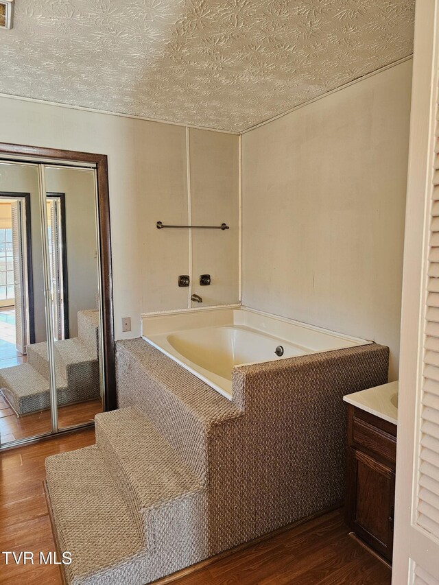 full bath with a textured ceiling, vanity, wood finished floors, and a bath