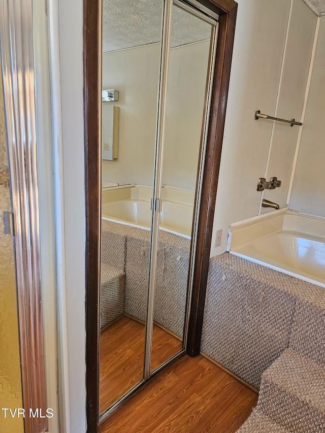 bathroom with a bathing tub, a textured ceiling, a shower, and wood finished floors