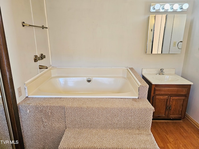 full bath featuring wood finished floors, a garden tub, and vanity