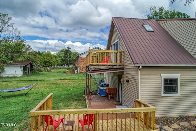 rear view of property featuring metal roof, a lawn, a wooden deck, and fence