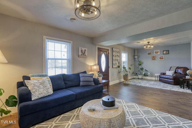 living area with an inviting chandelier, plenty of natural light, visible vents, and wood finished floors