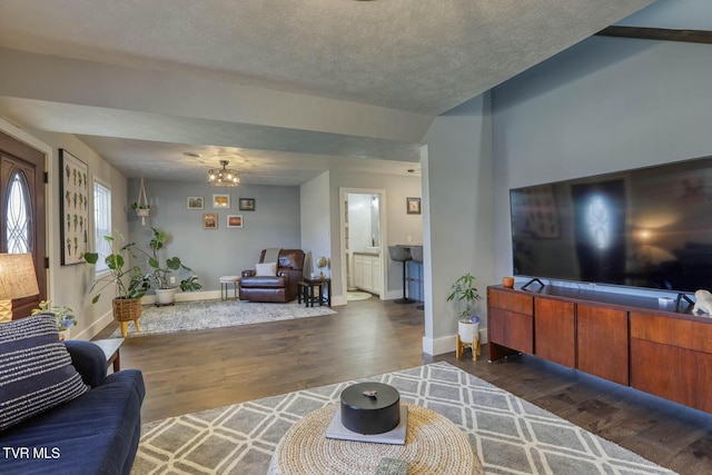 living room with dark wood-type flooring, a textured ceiling, baseboards, and an inviting chandelier