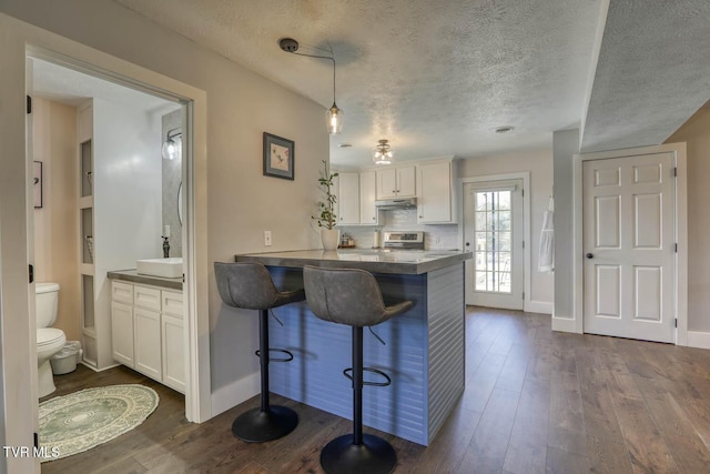 kitchen with under cabinet range hood, a peninsula, a kitchen breakfast bar, white cabinets, and hanging light fixtures