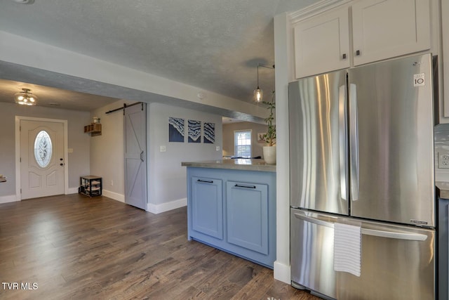 kitchen with dark wood finished floors, light countertops, a barn door, freestanding refrigerator, and white cabinetry