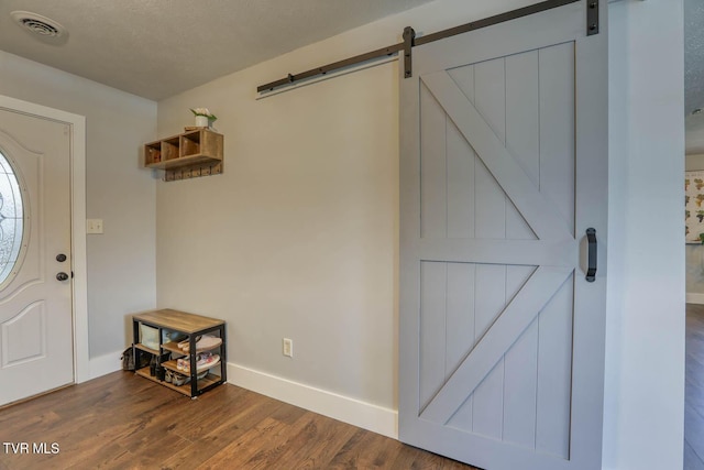 entryway with a barn door, visible vents, dark wood finished floors, baseboards, and a textured ceiling