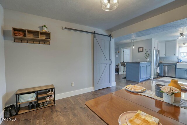 dining space with dark wood-style flooring, a textured ceiling, baseboards, and a barn door