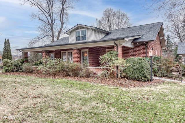 view of front facade with a porch, brick siding, roof with shingles, and a front yard