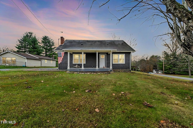 bungalow-style house featuring covered porch, a lawn, and a chimney