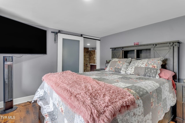 bedroom with dark wood-style floors, a barn door, and baseboards