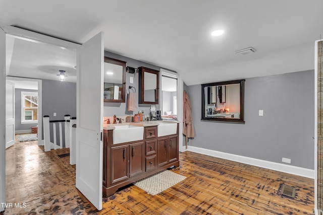 kitchen featuring wood finished floors, a sink, visible vents, baseboards, and light countertops