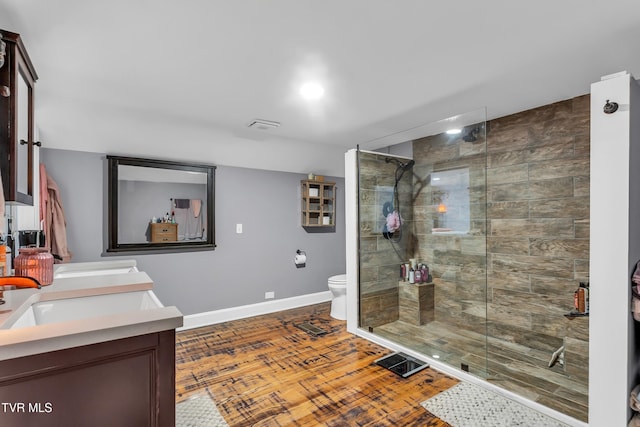 full bathroom with double vanity, toilet, wood finished floors, a walk in shower, and a sink