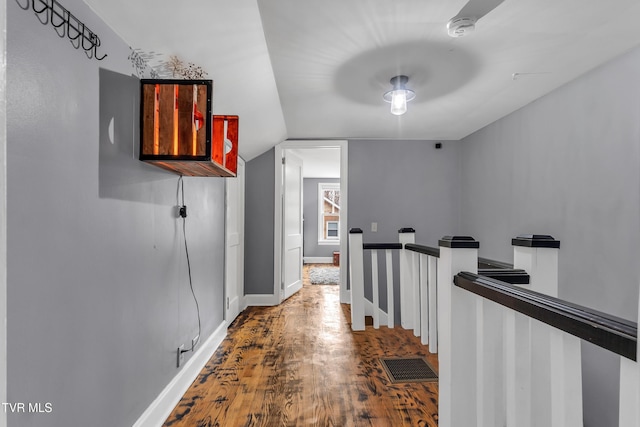 hall featuring wood finished floors, visible vents, an upstairs landing, vaulted ceiling, and baseboards