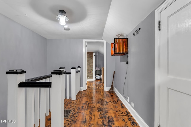 corridor featuring baseboards, dark wood-type flooring, and an upstairs landing