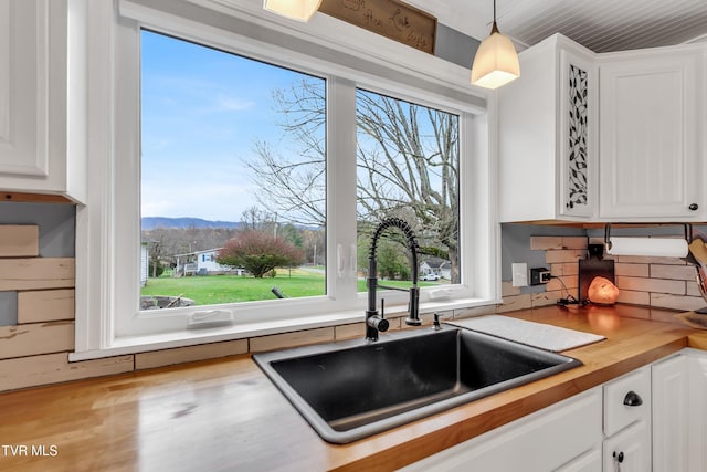 kitchen with white cabinets, wood counters, hanging light fixtures, a mountain view, and a sink