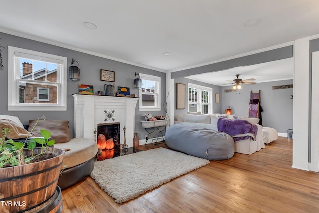 living area featuring baseboards, ornamental molding, a brick fireplace, and light wood-style floors